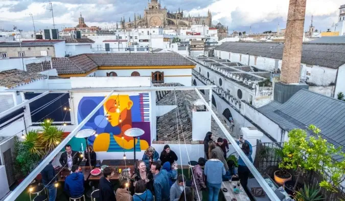 Emberek buliznak a La Banda Rooftop Hostel tetején, a háttérben a spanyolországi Sevilla látképével