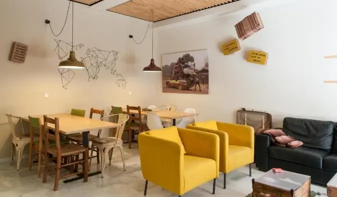 A The Nomad Hostel eklektikus közös területe fából készült asztalokkal és élénksárga nyugágyakkal Sevillában, Spanyolországban