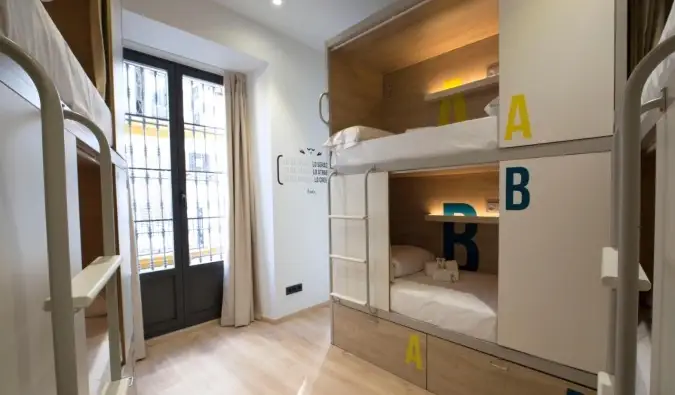 Modern pod stílusú emeletes ágyak egy erősen megvilágított szobában a For You Hostel Sevillában, Spanyolországban