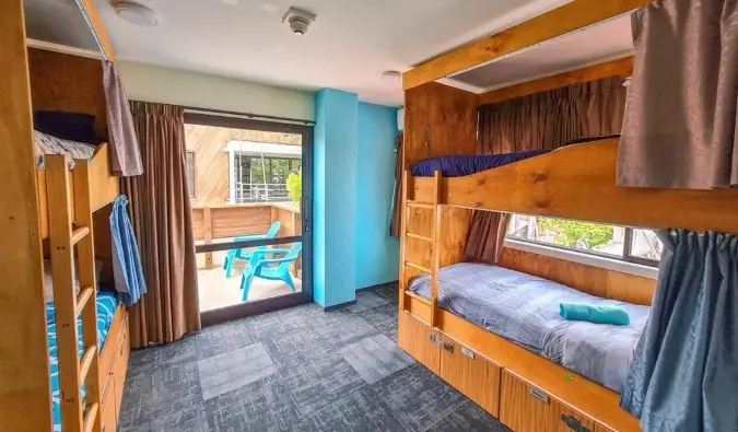 Lits superposés en bois avec rideaux d'intimité dans une pièce lumineuse de l'Adventure Queenstown Hostel à Queenstown, Nouvelle-Zélande