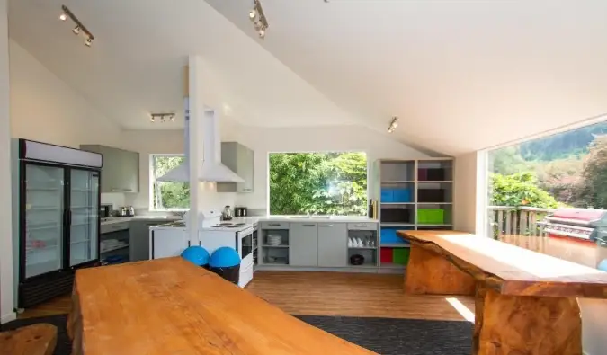 Vaste espace commun avec de longues tables en bois, un coin cuisine et d'immenses fenêtres au Haka Lodge à Queenstown, Nouvelle-Zélande