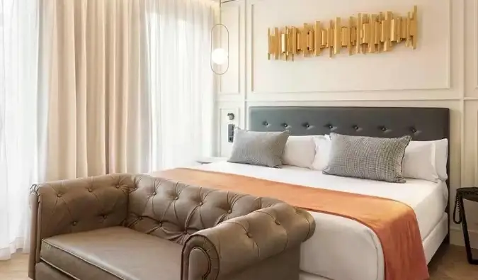 Une pièce de décoration dorée est suspendue au-dessus d'un lit double avec une causeuse au pied du lit de l'hôtel Catalonia Goya à Madrid, Espagne