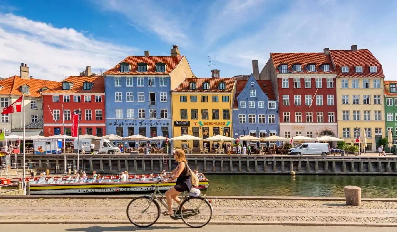 Une femme faisant du vélo près de bâtiments historiques colorés bordant un canal à Indry By, le centre historique de Copenhague, Danemark