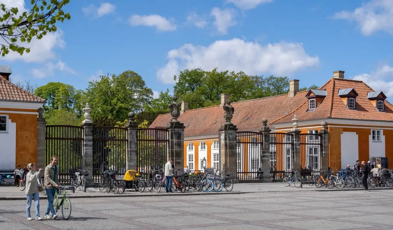 Passants devant une grande entrée fermée dans un parc arboré, flanqué de bâtiments historiques orange à Copenhague, au Danemark