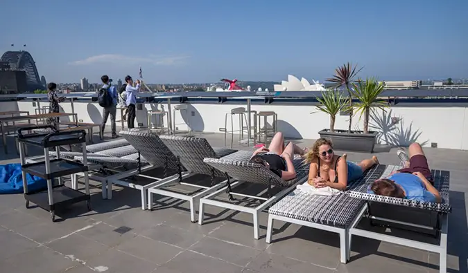 Terraço na cobertura com pessoas tomando sol nas espreguiçadeiras do albergue Sydney Harbour YHA em Sydney, Austrália