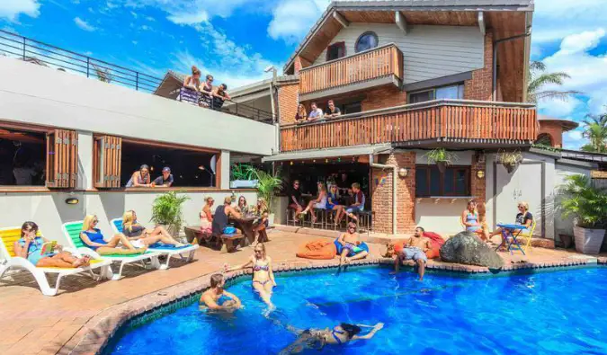 Pessoas nadando e descansando à beira da piscina do Aquarius Backpackers em Byron Bay, Austrália.