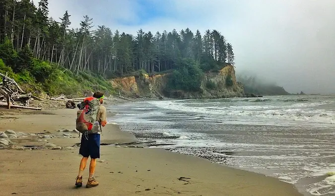 um mochileiro caminhando em uma praia isolada cercada por árvores
