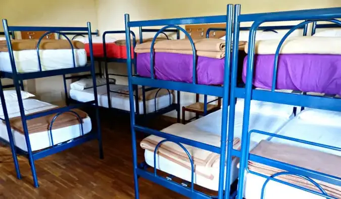 Un dortoir d'auberge rempli de lits superposés en métal bleu grinçant