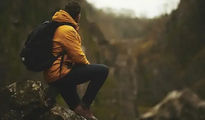 Um caminhante solitário com uma jaqueta amarela sentado nas montanhas olhando a paisagem ao seu redor