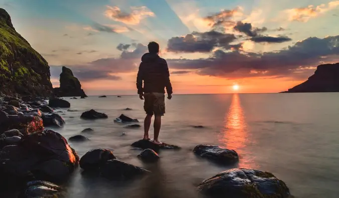 Um viajante solitário posando para uma foto melancólica ao pôr do sol enquanto está na praia