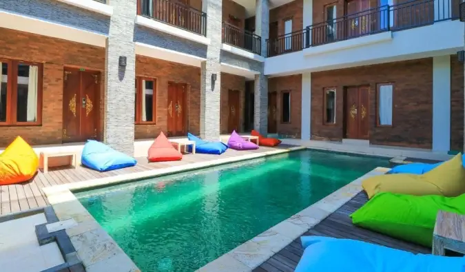 Longue piscine de couleur émeraude entourée de poufs colorés dans une cour intérieure du Gelatik Bed & Breakfast à Seminyak, Bali
