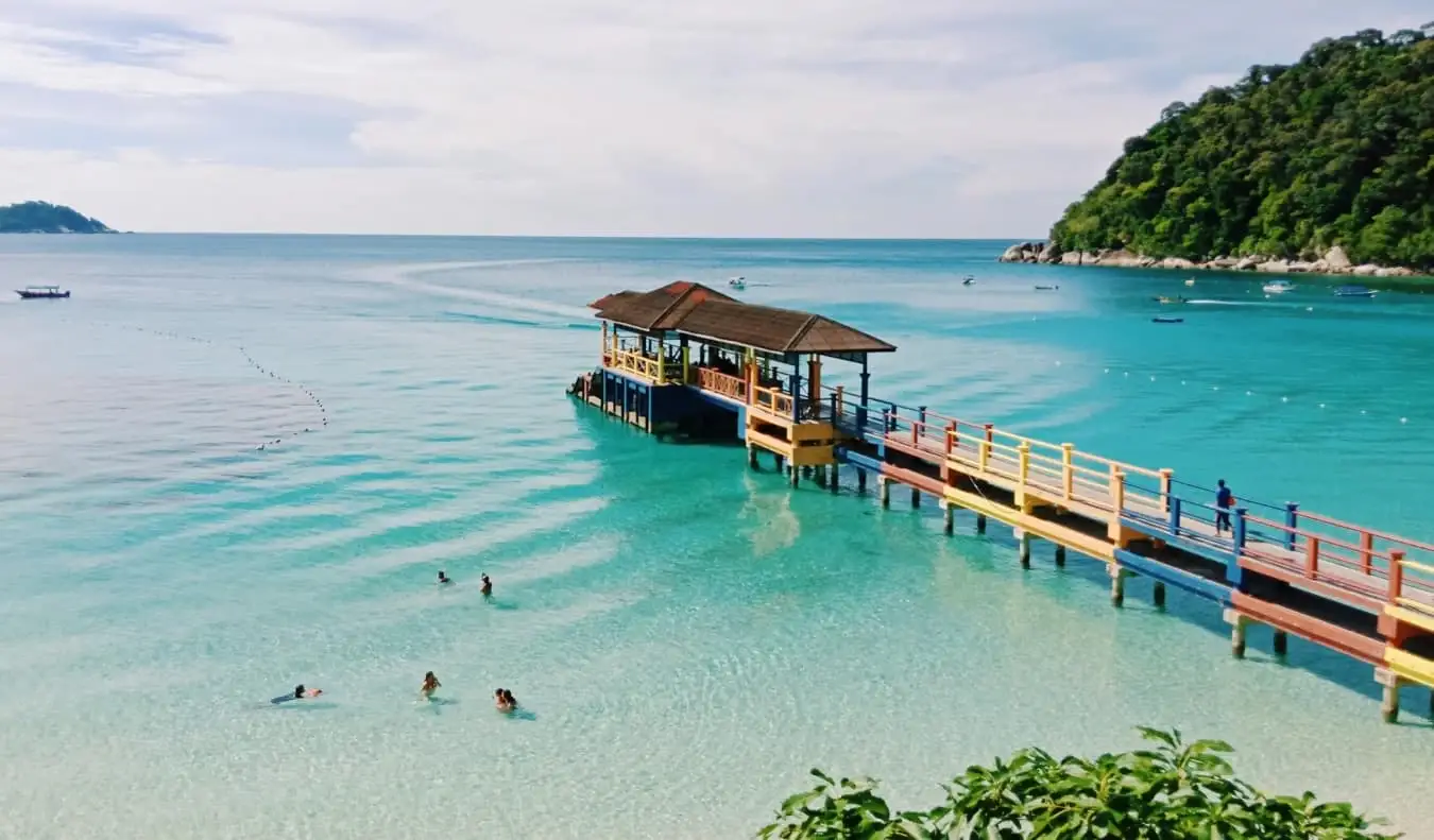 Cais colorido projetando-se nas águas azul-turquesa de uma praia nas Ilhas Perhentian, Malásia