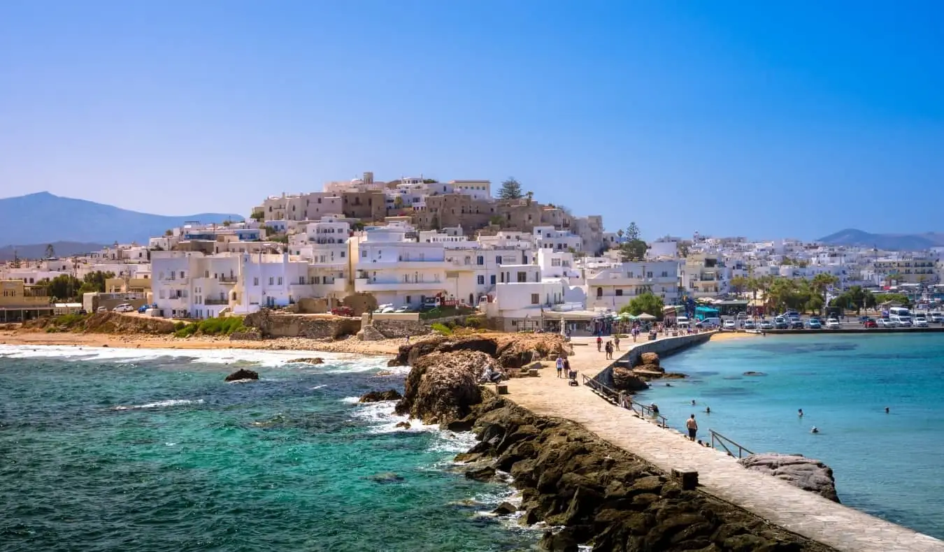 Pessoas andando por uma calçada de pedra que leva à cidade velha caiada de branco em Naxos, Grécia
