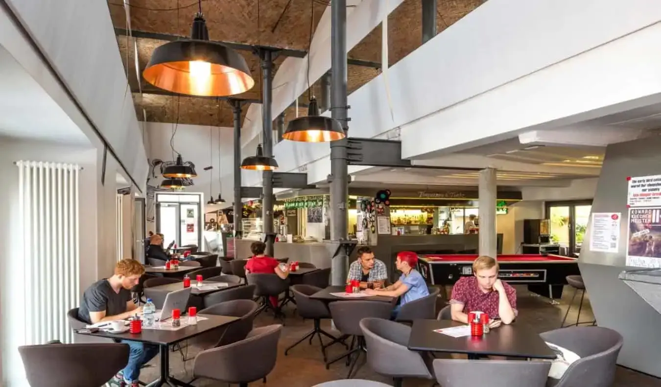 Espace commun avec de hauts plafonds et des personnes assises à des tables travaillant sur des ordinateurs portables et parlant à l'auberge Pfefferbett, Berlin