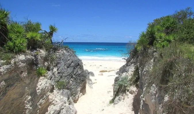 Entrée de sable de la plage des Caraïbes flanquée de deux gros rochers herbeux