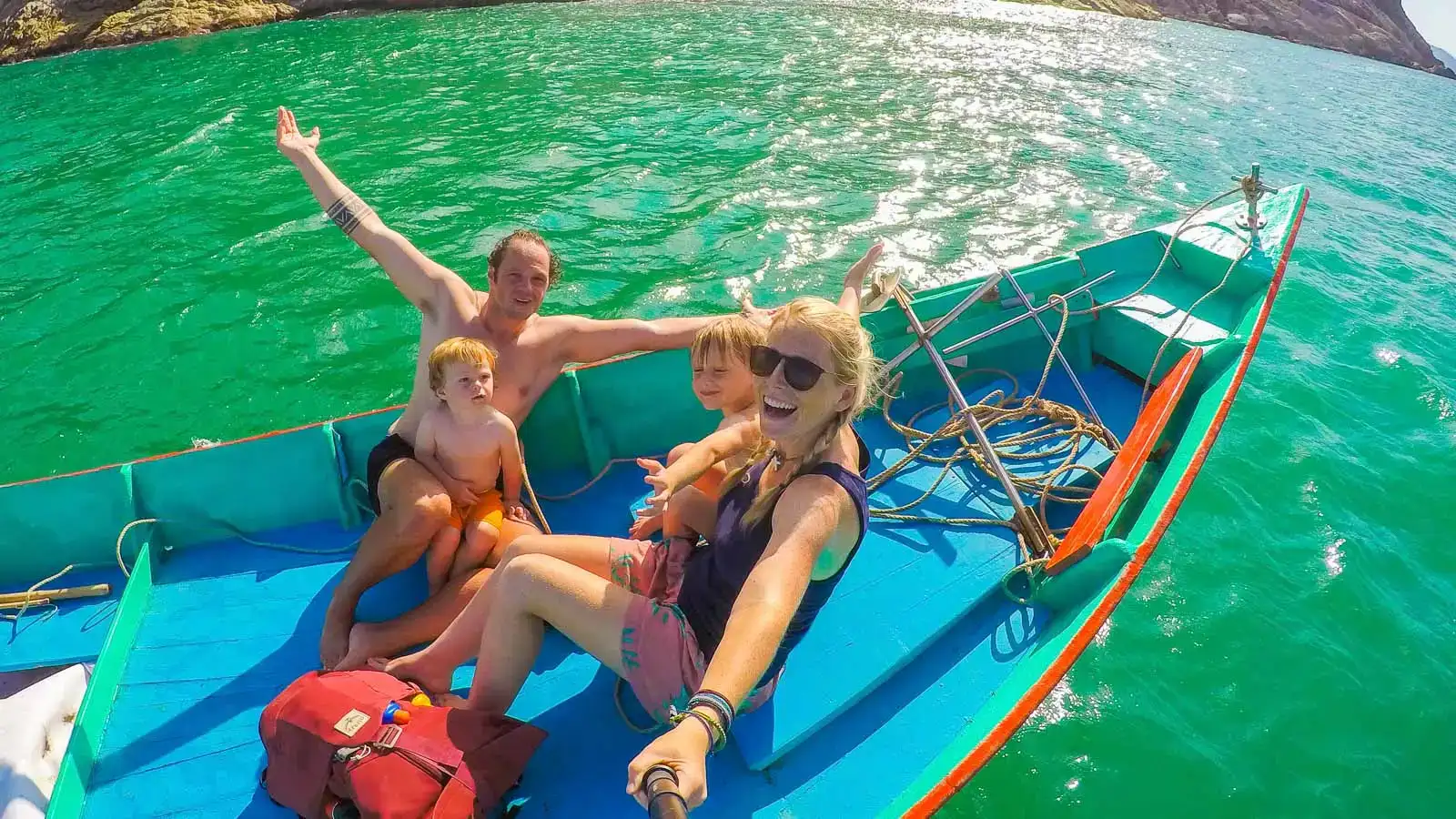 casal em pé em uma praia tropical deslumbrante com uma criança em cada ombro