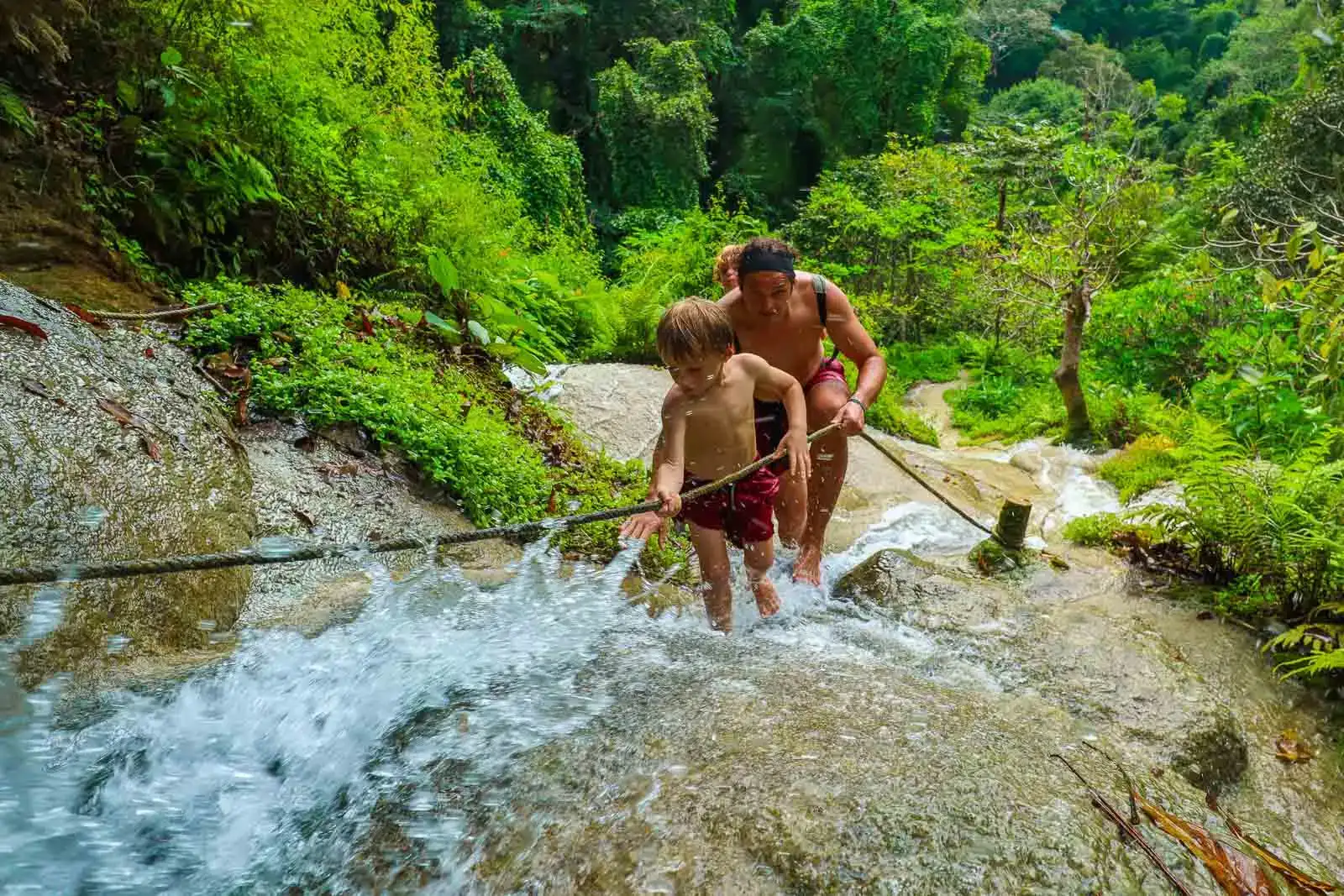 criança pequena e pai subindo uma cachoeira com uma corda