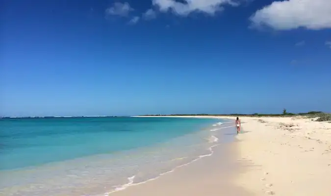 Uma pessoa caminhando pela ampla praia arenosa de Anegada
