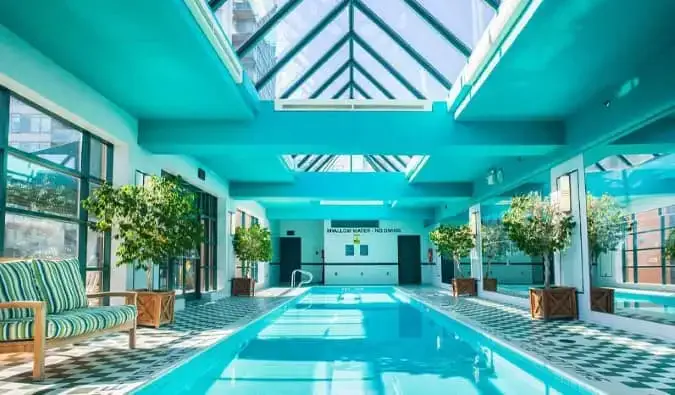 Uma longa piscina coberta cercada por pequenos vasos de árvores em um átrio de vidro no hotel Yorkville Royal Sonesta em Toronto, Canadá