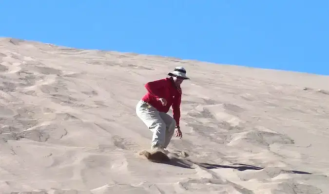 Um viajante de 50 anos descendo uma duna de areia