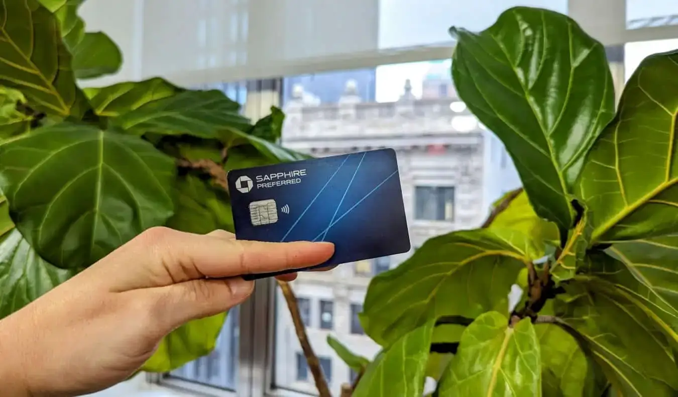 La Chase Sapphire Preferred Card est présentée devant une plante feuillue avec des bâtiments visibles à travers la fenêtre en arrière-plan