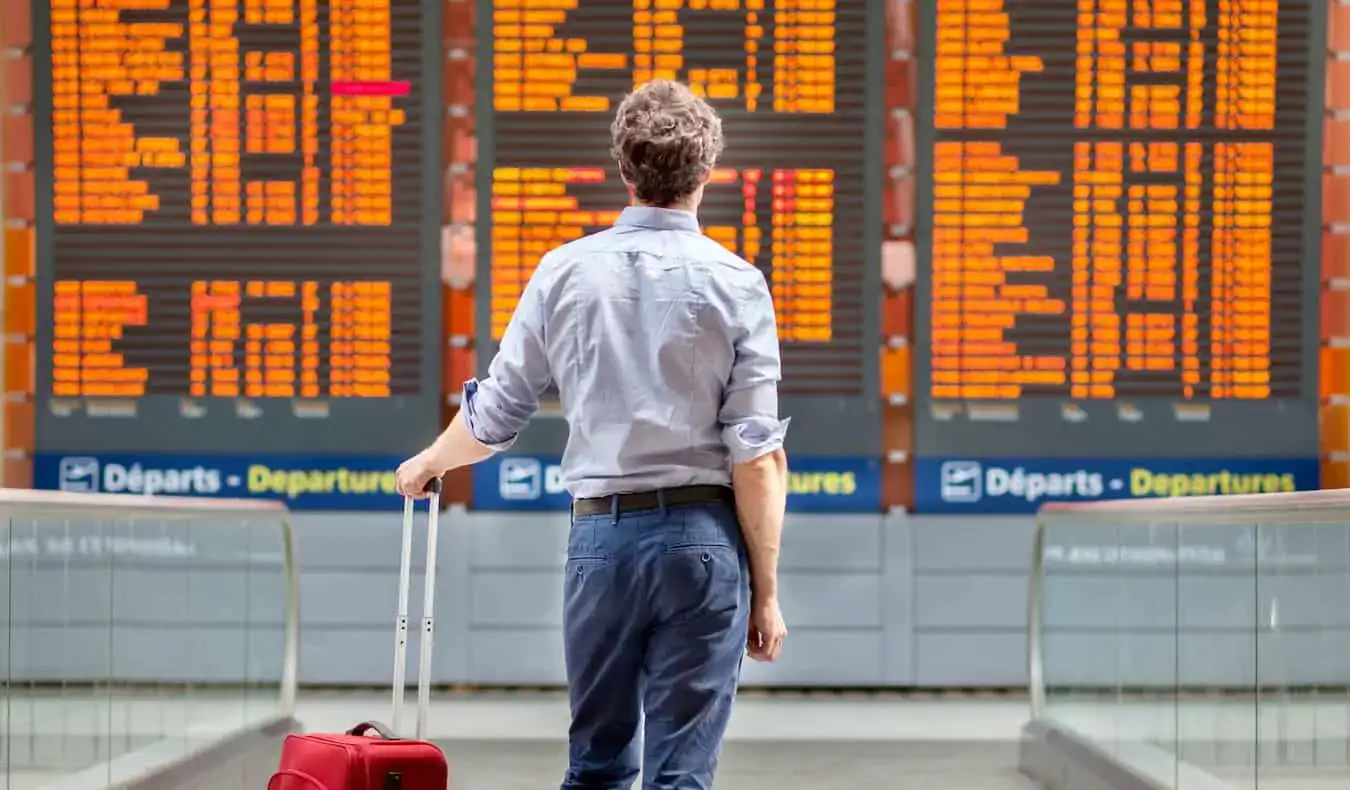 Um homem parado ao lado de sua bagagem olhando para uma placa de voo do aeroporto