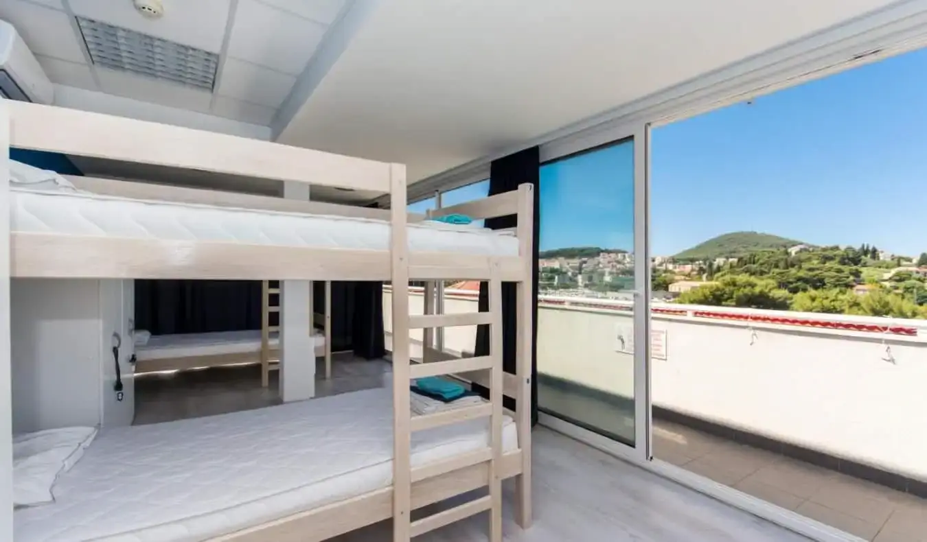 Lits superposés avec portes coulissantes en verre ouvrant sur un balcon donnant sur les collines luxuriantes de l'auberge Petra Marina à Dubrovnik, en Croatie.