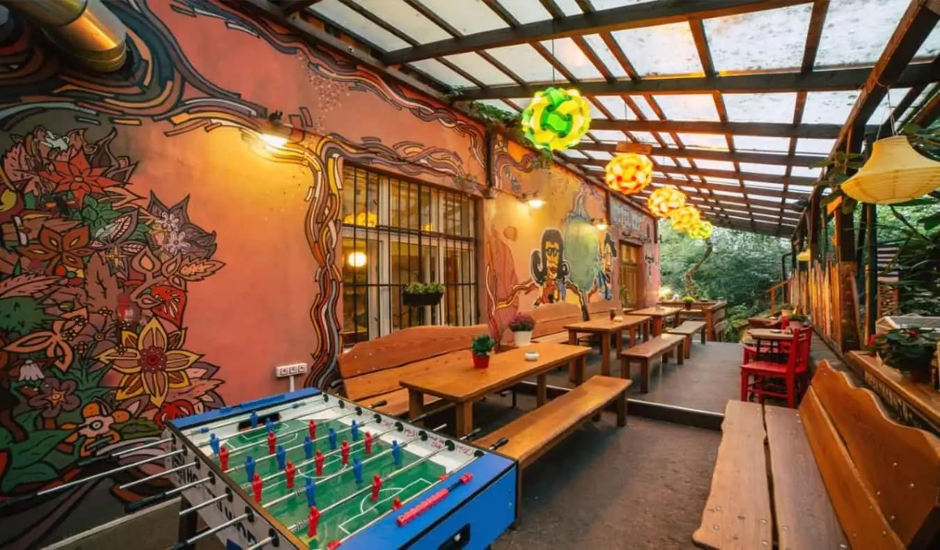 Café en plein air couvert avec de longues tables et bancs de pique-nique en bois, une table de baby-foot et des peintures murales peintes sur le bâtiment de l'auberge Elf à Prague.