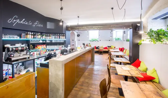 Coin café avec bar et beaucoup de tables, bancs et chaises en bois chez Sophie