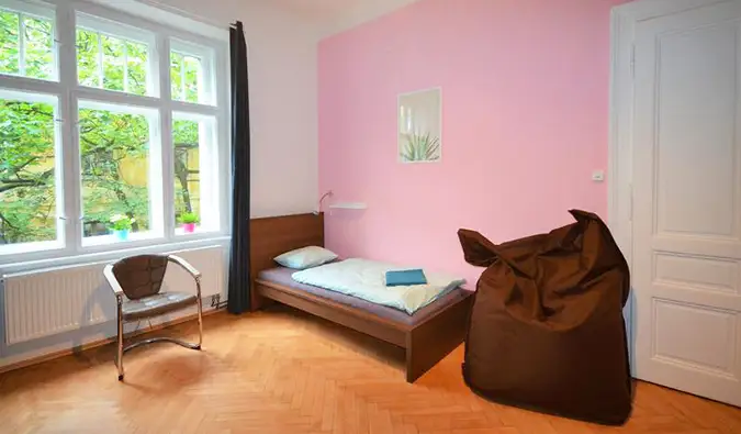 Chambre avec murs roses, fauteuil poire, lit jumeau et grandes fenêtres au Travel and Joy Hostel à Prague
