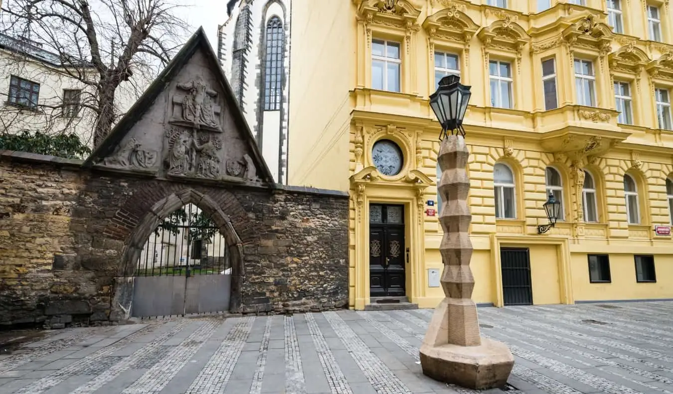 Lampadaire cubiste devant un bâtiment jaune historique et une arcade fermée, à Prague, en République tchèque