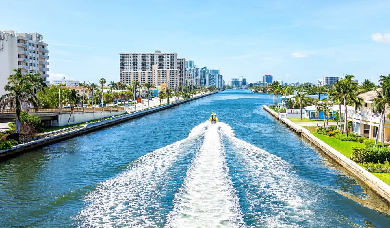 Sebuah perahu berlayar menyusuri kanal besar yang dipenuhi gedung apartemen dan pohon palem di Miami, Florida