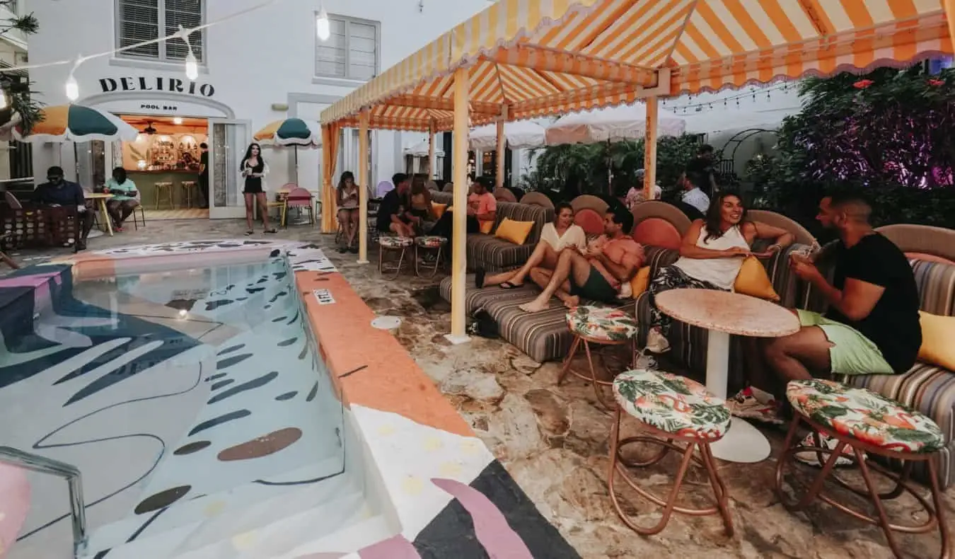 Des gens assis à de petites tables à côté d'une piscine extérieure avec des carreaux colorés à l'auberge Viajero à Miami, en Floride