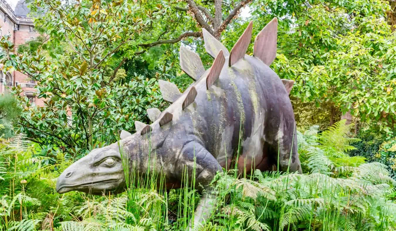 En dinosaurstatue i høyt gress i Paris, Frankrike