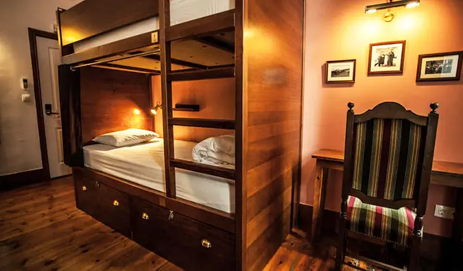 Lits superposés en bois sombre et bureau avec chaise dans un dortoir du Home Lisbon Hostel