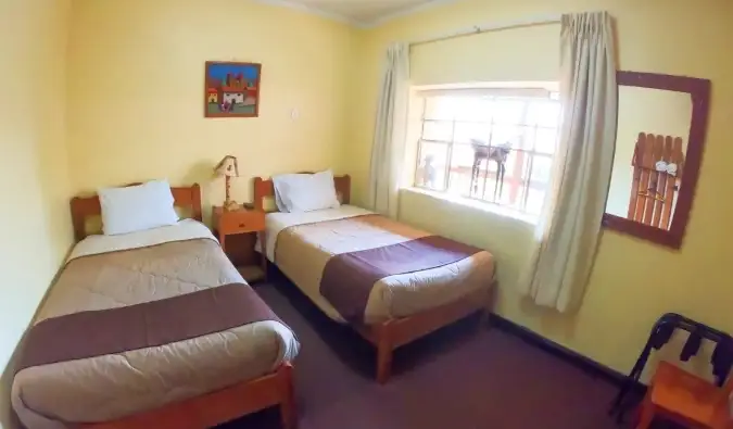 Lits jumeaux dans une chambre jaune simple à l'Hospedaje Turístico Recoleta, une auberge de jeunesse à Cusco, Pérou