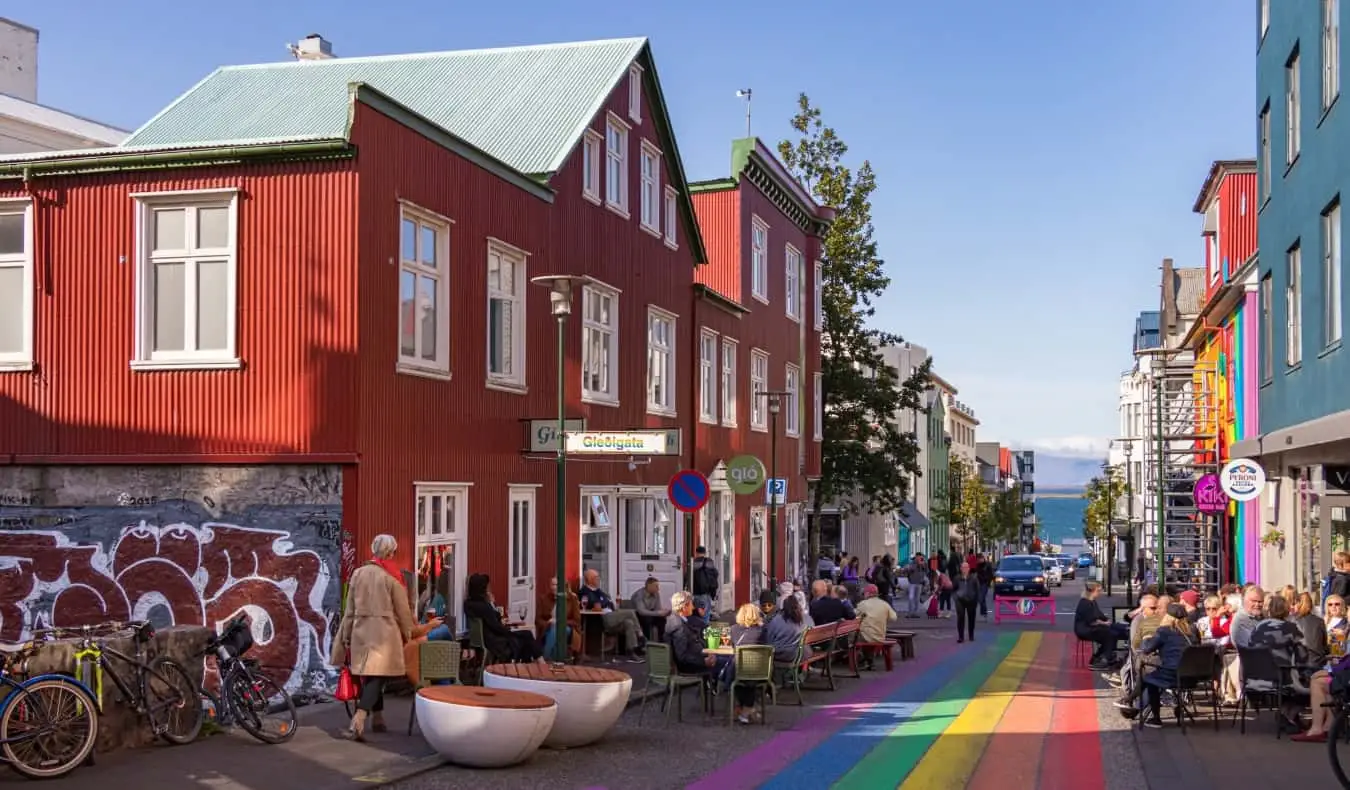 Uma paisagem urbana em Reykjavik, Islândia, com pessoas sentadas em cafés ao longo da rua pintada com arco-íris