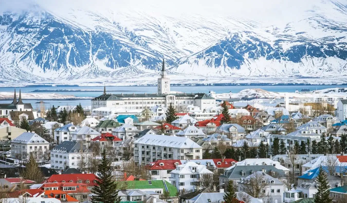 Horizonte da cidade de Reykjavik com telhados coloridos, uma torre de igreja e montanhas cobertas de neve ao fundo na Islândia