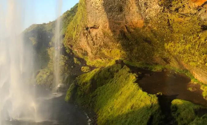 Seljalandsfoss užpakalinė dalis su puikia šviesa, vandeniu, mėlynu dangumi ir žaluma