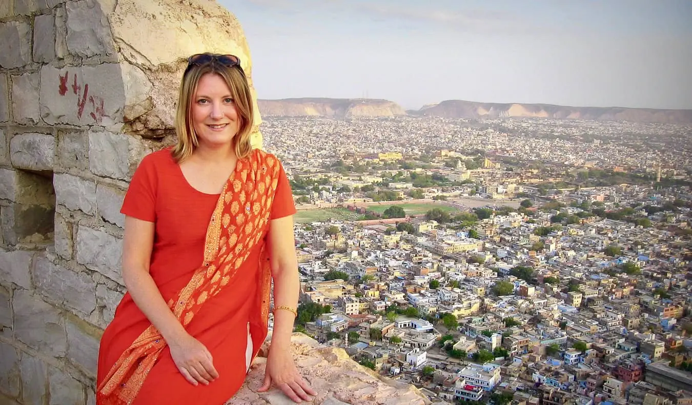 Uma viajante solitária na Índia posando perto de um muro histórico com vista para uma cidade
