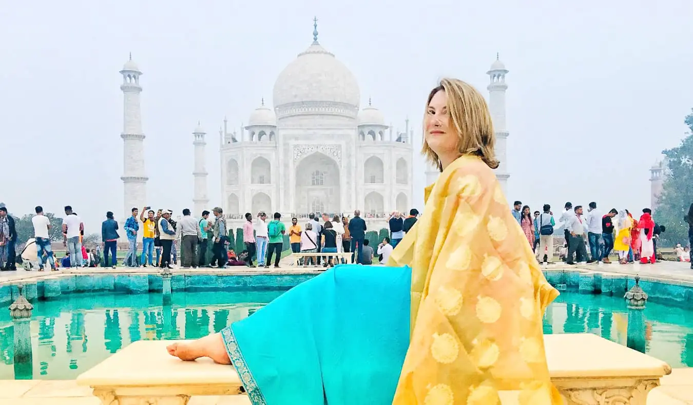 Uma viajante solitária em um sári colorido posando em frente ao Taj Mahal, na Índia