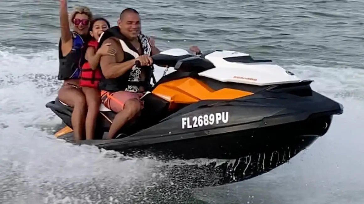 Семья из трех человек на оранжевом водном мотоцикле в Майами, Флорида, улыбается.