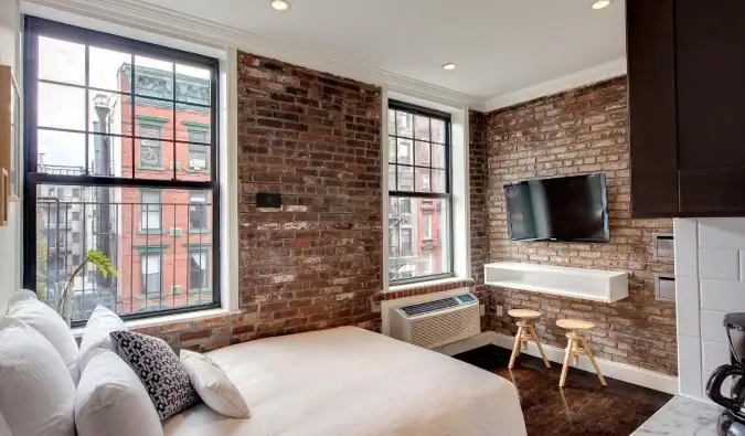Chambre d'hôtel ensoleillée avec murs en briques apparentes, lit double et télévision à écran plat sur les murs de l'East Village Hotel à New York