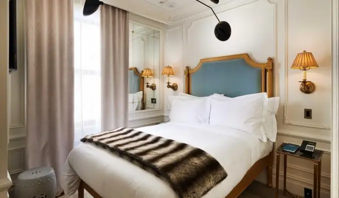 Chambre d'hôtel majestueuse avec une tête de lit dorée, des lampes de chaque côté du lit et des moulures blanches sur les murs de l'hôtel Marlton à New York