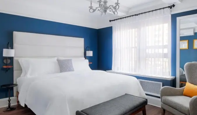 Chambre d'hôtel simple avec des murs d'un bleu profond, un lustre et une chaise assise à côté d'un lit queen-size à l'hôtel voco The Franklin à New York