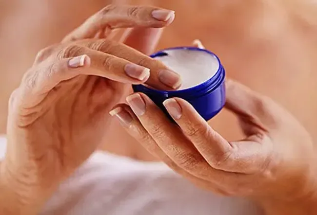 A woman putting thick cream onto her hands.