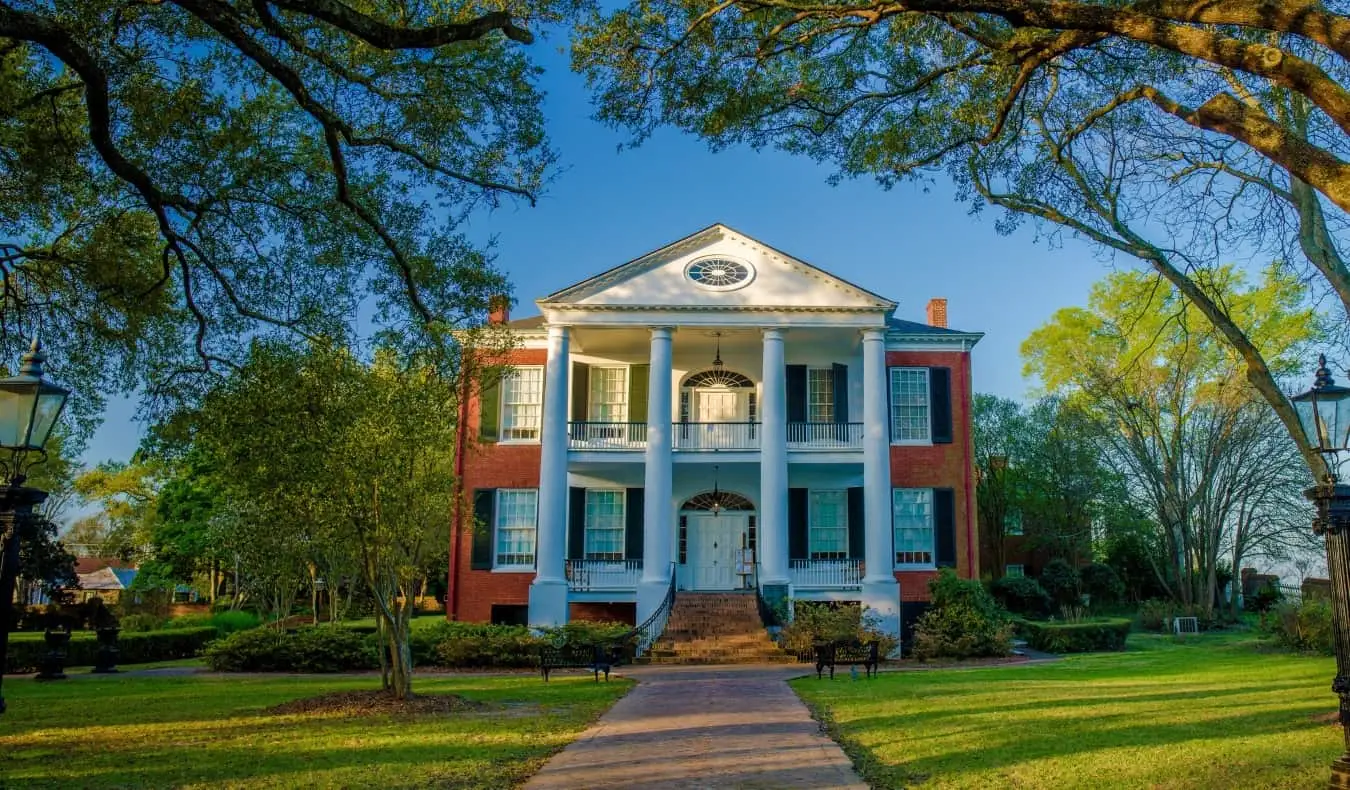 Um caminho que leva à histórica mansão Rosalie, com pilares brancos e fachada de tijolos com venezianas de madeira preta, cercada por árvores exuberantes em Natchez, Mississippi, EUA