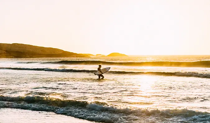 Um viajante solitário surfando na África do Sul enquanto o sol se põe ao fundo