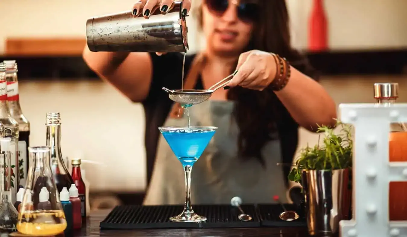 En kvinnelig bartender skjenker en fargerik drink i baren